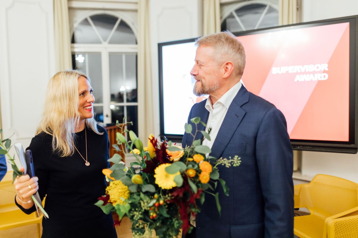 enlarge the image: Two award winners of the supervisor award smile at each other with flowers in their hands.