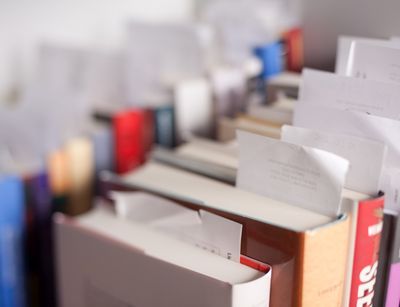 mehrere Bücher stehen nebeneinander und hintereinander im Regal, darin sind Zettel geklebt, Sicht von leicht oben